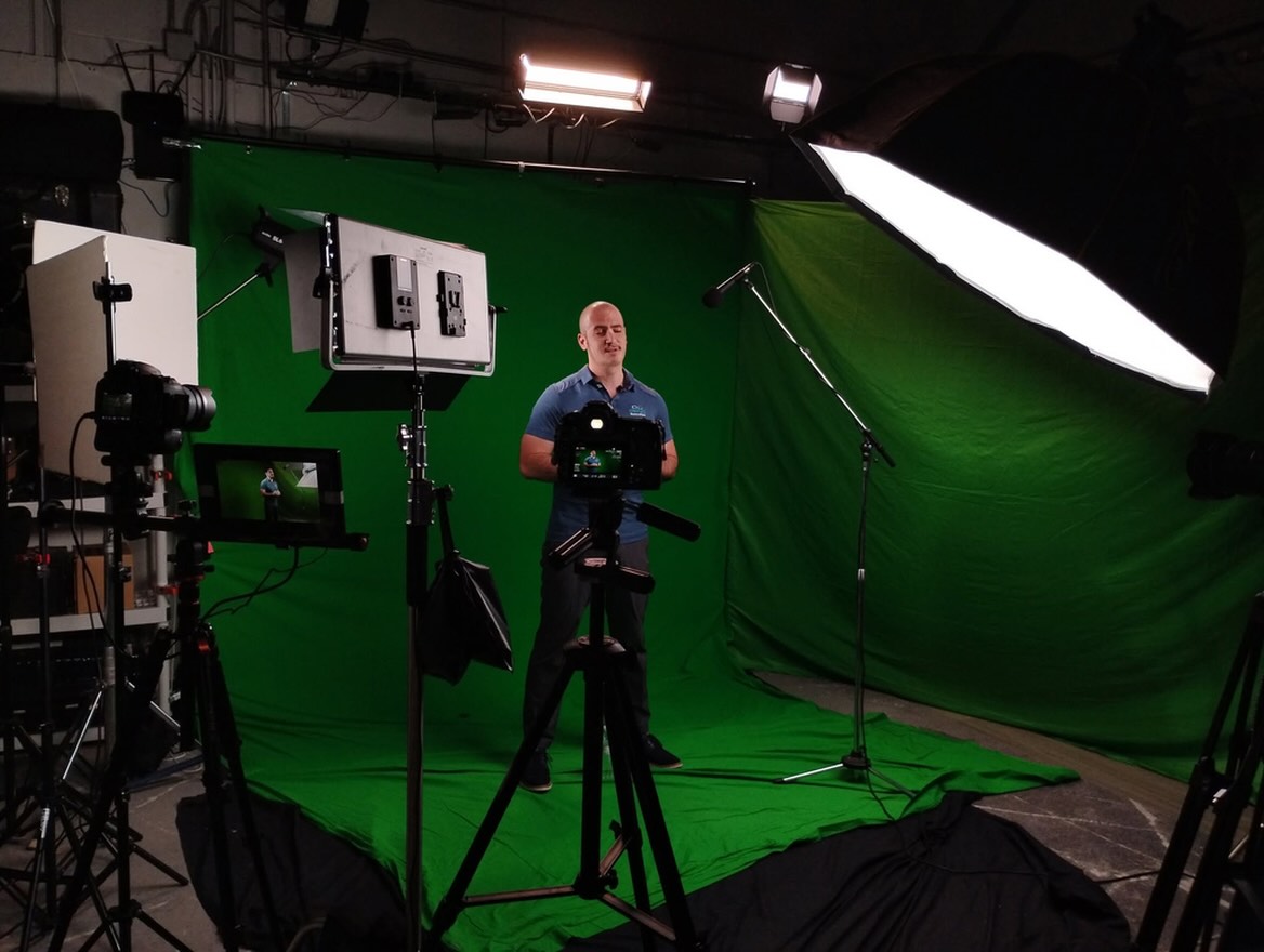 On-camera host on the green screen stage at the Elated Dallas studio, framed by cameras and lights