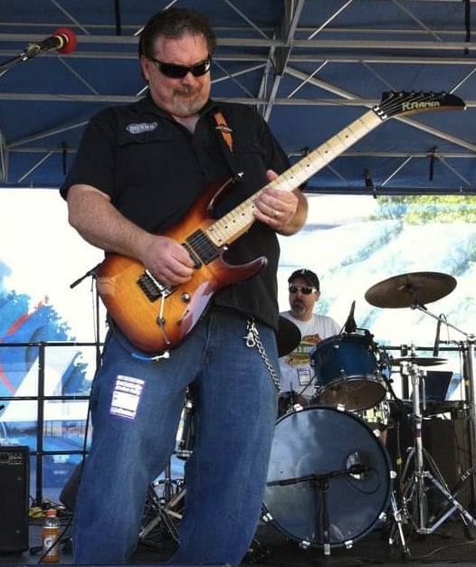 Guitarist playing a sunburst electric guitar on an outdoor festival stage